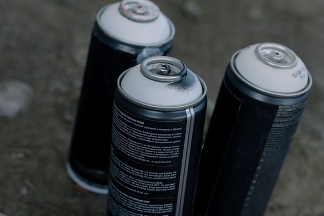 Three used aerosol spray cans standing on bare stony ground.