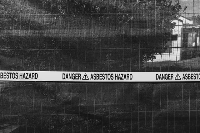 Danger asbestos hazard tape stretched across a fence around a building site, in black and white.