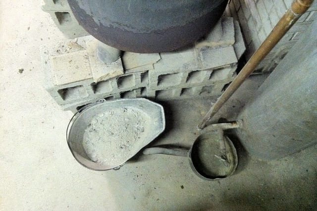A metal pan of grey ash taken out of an old stove, beside a shovel.