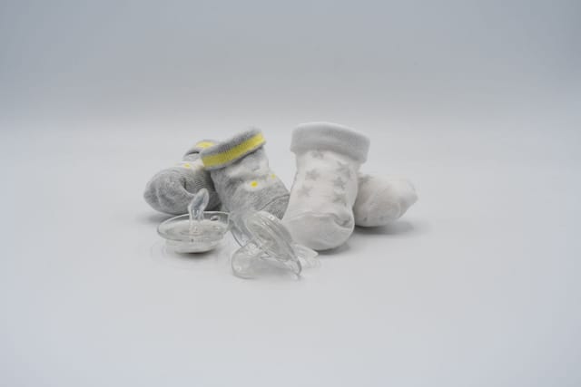 A pair of small baby socks and a dummy on a plain grey background.