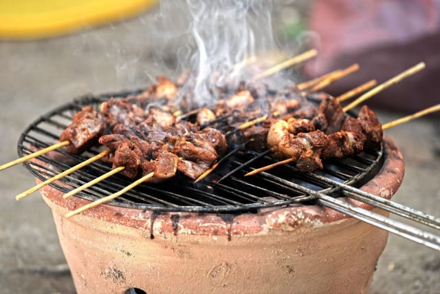 Skewers of meat cooking on a small round clay barbecue grill.