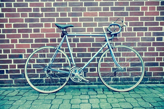 A silver road bicycle leaning against a red brick wall.