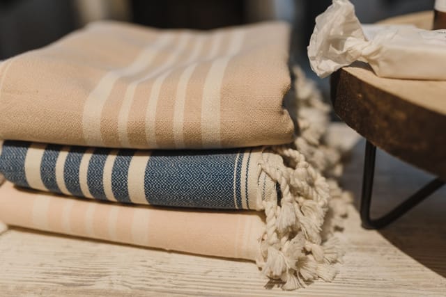 Folded striped cotton blankets with tasselled ends stacked on a wooden surface.