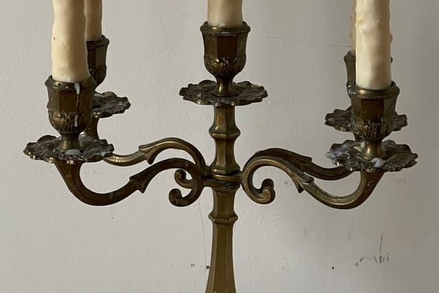 Three tall white candles in plain holders standing against a pale wall.