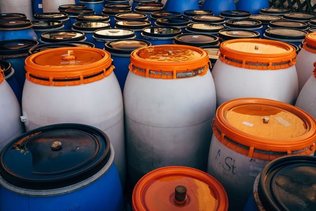 Rows of white and blue plastic chemical drums with orange lids.