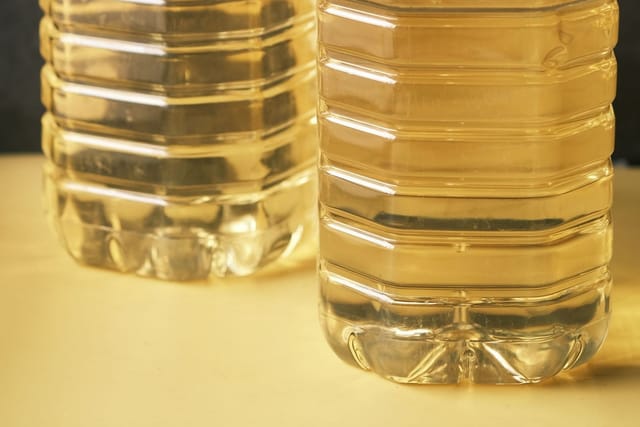 Two large plastic bottles of cooking oil with yellow caps and white handles.