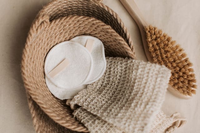 Reusable cotton make-up pads and a washcloth in a rope basket beside a wooden brush.