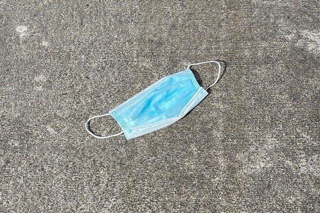 A used blue disposable face mask lying on a concrete pavement.