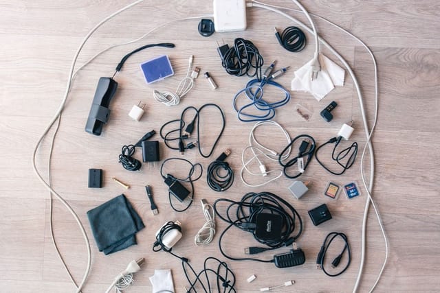 Old chargers, cables, plugs and small electrical gadgets laid out on a wooden floor.