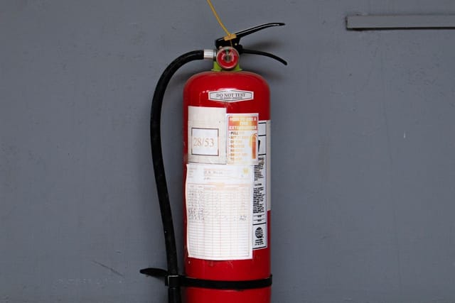 A red fire extinguisher hanging on a bracket against a grey wall.