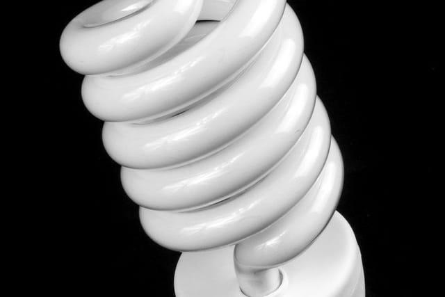Close-up of a white spiral energy-saving light bulb against a black background.