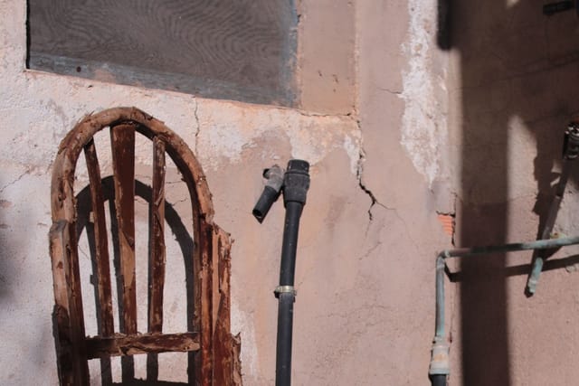A broken old wooden chair standing against a cracked plaster wall.
