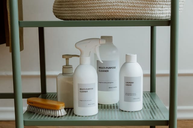 White bottles of multi-purpose cleaner and laundry liquid on a green metal shelf.