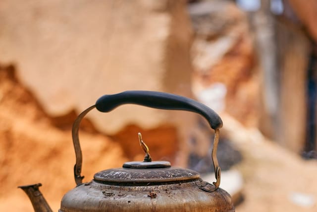 A blackened old metal kettle resting on a woven stand outdoors.