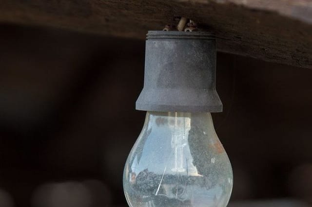 A clear old-style light bulb hanging from a worn metal holder.