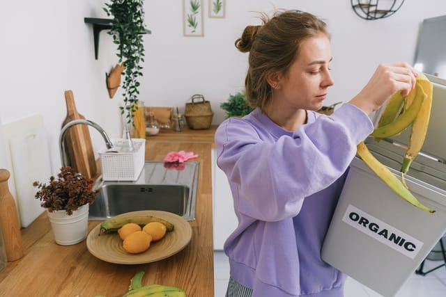 A woman drops banana peel into a small bin labelled ORGANIC in her kitchen.
