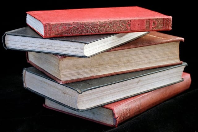 A stack of five old hardback books with worn red and grey covers against a black background.