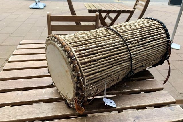 A traditional wooden drum bound with cord, lying on a wooden table outdoors.