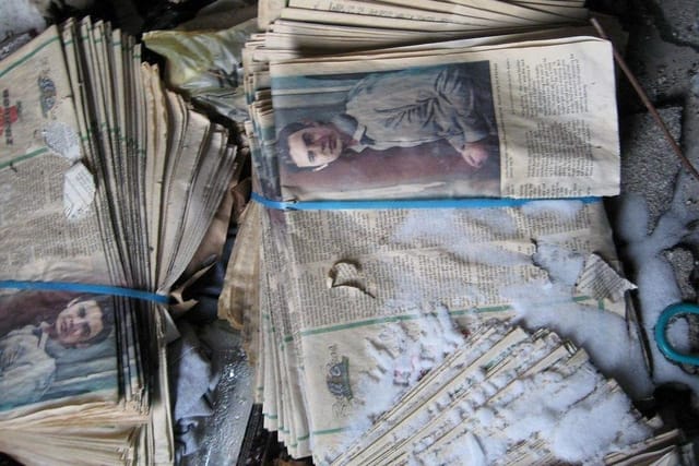 Bundles of old newspapers tied with string, lying in a heap.