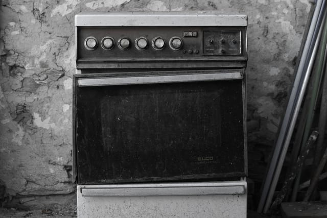An old free-standing cooker with an oven and control knobs, standing against a stone wall.