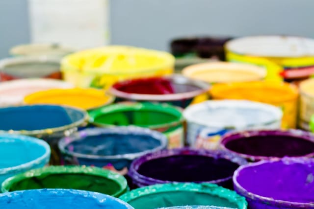 Many open tins of paint in bright colours crowded together.