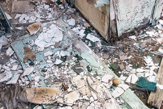 Broken plasterboard and building rubble on the ground beside a wooden structure.