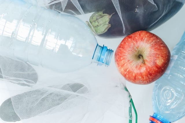 Plastic mesh produce bags holding peppers, beside an empty plastic bottle.