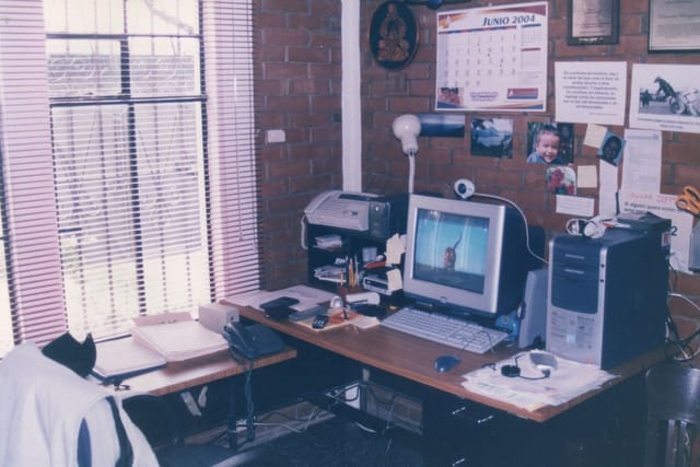 A home office desk with an old computer, monitor and printer by a window.