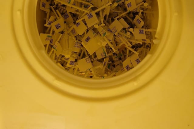Used syringes and needles inside a yellow sharps container, seen from above.