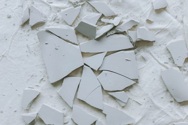 Broken pieces of pale grey tile scattered over a white surface.