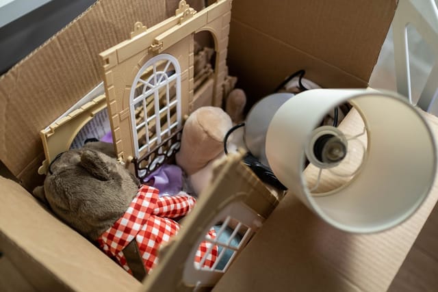 A cardboard box packed with a toy doll's house, soft toys and a lamp, ready to give away.