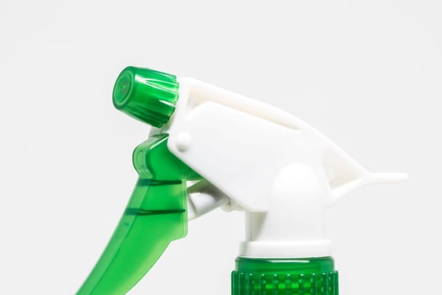 Close-up of the green and white trigger head of a plastic spray bottle on a plain white background.
