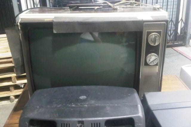 An old box television set with dials on the side, stored with other old electrical goods.