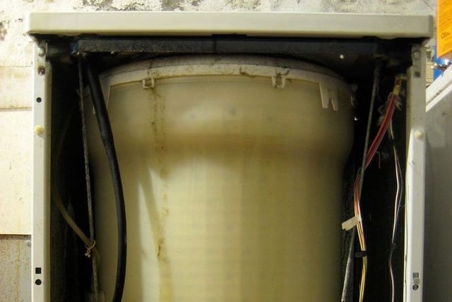 An old washing machine with its casing removed, showing the drum and wiring inside.