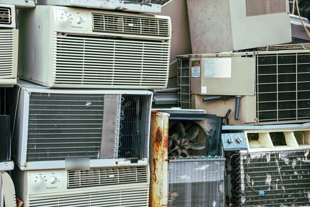 Old window air conditioning units stacked on top of one another in a scrapyard.